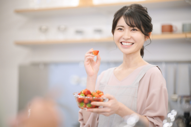 イチゴを片手に微笑む女性の画像
